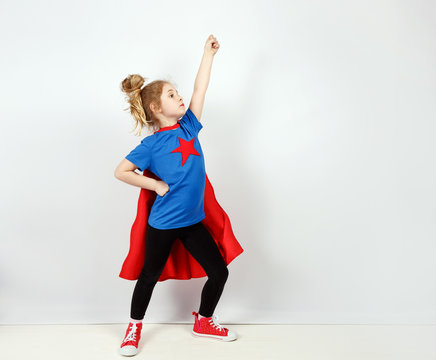Six year blonde girl dressed like superhero having fun at home. White wall on background