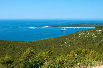 Fotobehang One ship and several yachts in the azure blue sea in a bay near the coast of an island with hills covered in green verdant forest. Blue cloudless sky. Dugi otok, Croatia © shinedawn