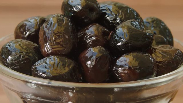Circular movement of the camera around black olives in glass bowl.