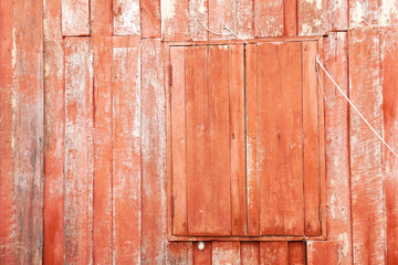 Red painted wood of old traditional wooden thai house with closed window, red background, closeup and detail of weathered wood 