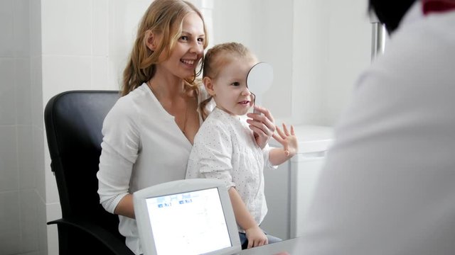 Pretty girl closes one eye - Optometrist in clinic checking little child's vision