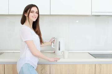 Pretty girl pours water from the kettle in the kitchen