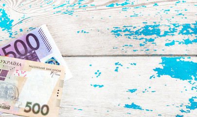 500 euro and 500 hryvnia bills on the old blue wooden background.