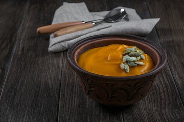 Pumpkin cream soup with seeds  in a clay bowl on dark wooden  table