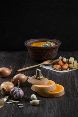 Pumpkin and ingredients for cooking over dark wooden  background.  Fresh pumpkin slice, garlic,onion. Pumpkin cream soup
