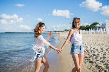 Pretty girl walking on beach holding hand with her friend