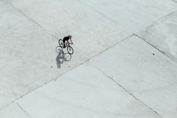 Small  fast fit strong professional female cyclist riding through concrete metropolitan park white light shadow shot from above
