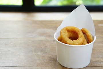 Fried onion rings in a cup on wooden table with copy space.