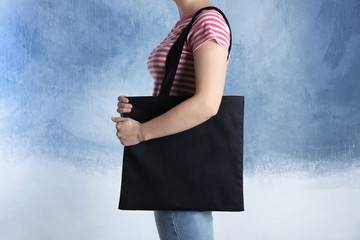 Young woman with shopping bag on color background