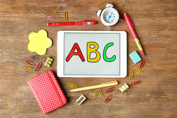 Tablet with ABC message and stationery on wooden background