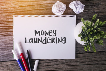 Money Laundering word with Notepad and green plant on wooden background.