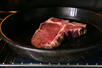 Pan with raw steak in oven