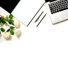 Modern minimalistic work place. White office desk table with laptop keyboard, pen, white roses. Top view with copy space, flat lay