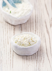 Rustic white bowl of homemade cottage cheese on a wooden marble table with copy space. Selective focus.