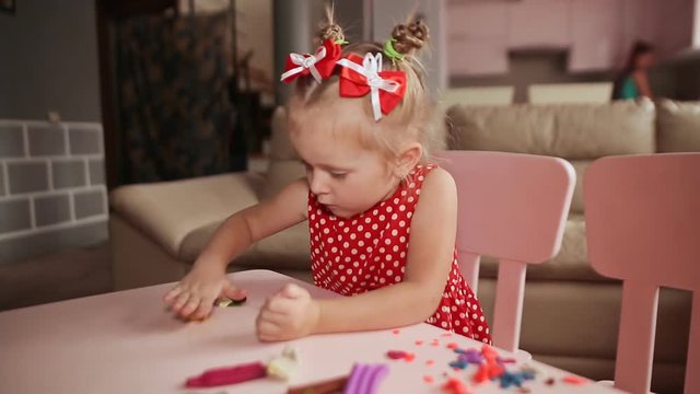 A charming little girl sculpts from plasticine at a table in her room.