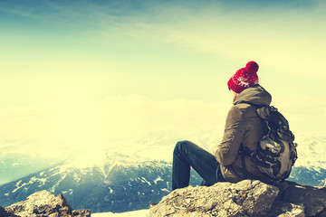 Young sportsman or traveler sitting on stone and looking on horizon. Mountain range on background....