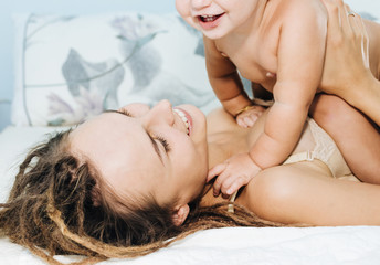 Mom and baby on the bed. A woman and her todler are playing lying in the bedroom.