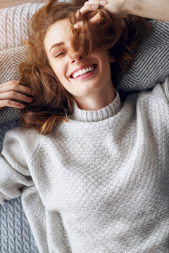 The concept of a lifestyle. Young beautiful sexy girl in a sweater lies on a bed and laughs