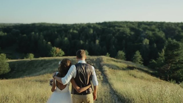 Young beautiful and happy couple bride and groom walking at sunset on the day of their wedding.Walk down the hill.