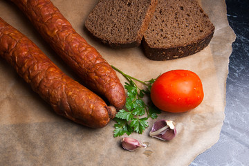 Close up view smoked sausage with spice, herbs and vegetables on the packaging paper.