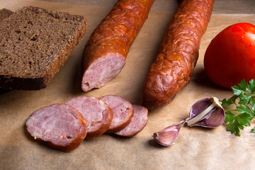 Slices of smoked sausage with spice, herbs and vegetables on the packaging paper.