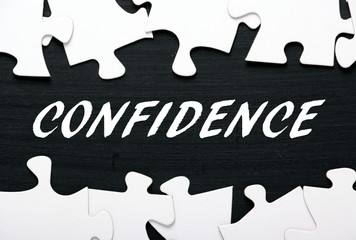 The word Confidence in white text on a blackboard with a border of jigsaw puzzle pieces as a metaphor for unlocking your potential