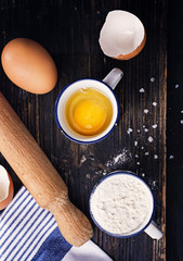 Black wooden surface with ingredients for classic pasta- egg flour salt. Free text space, top view.