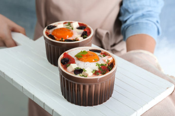 Female hands holding board with baked eggs with tomatoes and olives