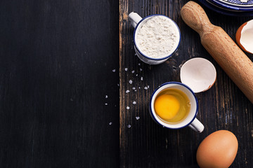 Black wooden surface with ingredients for classic pasta- egg flour salt. Free text space, top view.