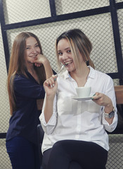 Two young girls have a cofee time at the counter in a cafe and talking and laughing