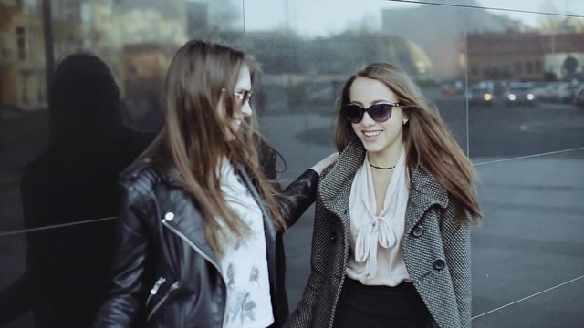 Two stylish brunette girls standing together on street, embracing, making face and smiling