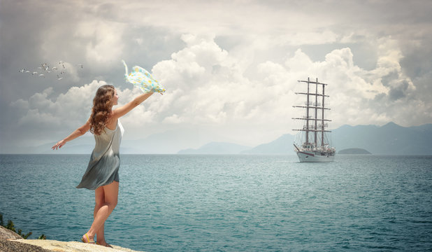 A happy romantic woman meets a sailing ship on the shore waving a handkerchief