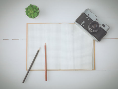 Top view image , open blank notebook, old camera on white wooden table