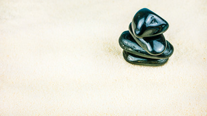 Fototapeta na wymiar Growing piled up of four black pebbles on bright white sand