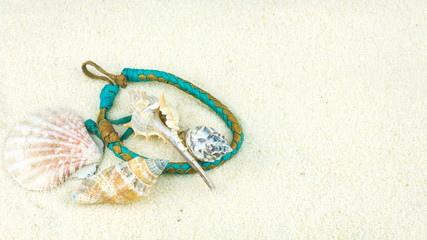 Sea shells and coloured wristbandon on sandy beach
