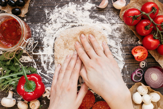 Woman preparing dough for pizza. Hands kneading dough on the wooden table, top view