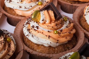Vanilla cupcakes with orange and white creamcheese and chocolate decor. Selective focus. Shallow depth of field