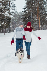 Fototapeta na wymiar Young couple with a Husky dog walking in winter park, man and woman playing and having fun with dog.