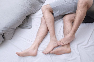 Legs of gay couple lying in bed