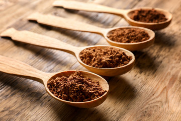 Spoons with cocoa powder on wooden background
