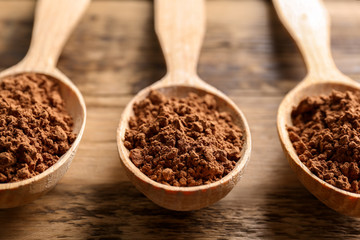 Spoons with cocoa powder on wooden background