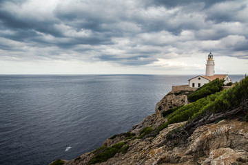 Fototapeta na wymiar Amazing lighthouse Cala Ratjada is located in the easternmost part of Mallorca on the cliff. Lighthouse in cloudy day with beautiful view on the ocean. Balearic Island Mallorca, Spain.
