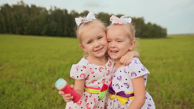 Cute happy little sister twins embrace fun outdoors in the summer.