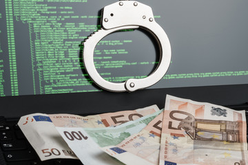 Handcuffs on the laptop and money on the keyboard. Cyber hacker crime concept.