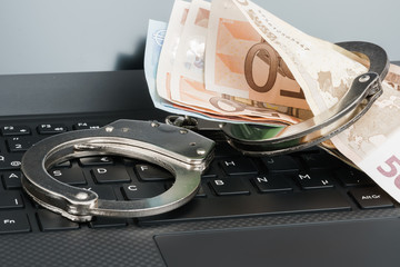 Money in handcuffs on the laptop keyboard. Cyber hacker crime concept.