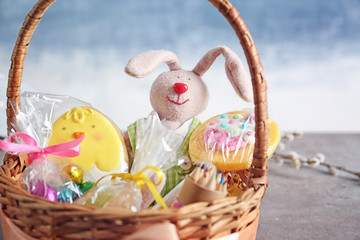 Easter basket with bunny toy and sweets on light background