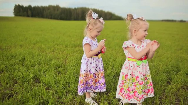 Two lovely little sisters twins in a meadow blow bubbles and give each other kisses.