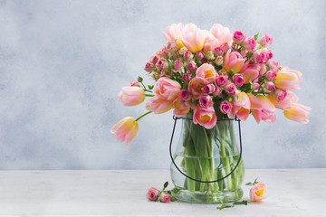 fresh pink and yellow tulips and roses in glass vase on gray background