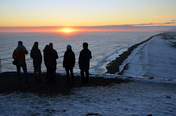 Gropu of young people watchingbeautiful sunset over the sea in vik - iceland