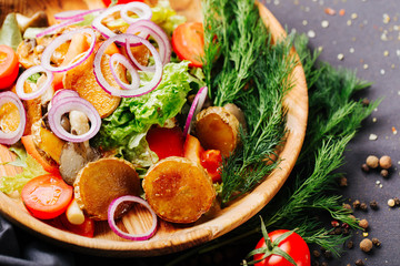 Close up of stir-fried vegetables, potatoes, pepper, tomato, onion and herb on a wood plate. Black background is decorated with pepper peas,